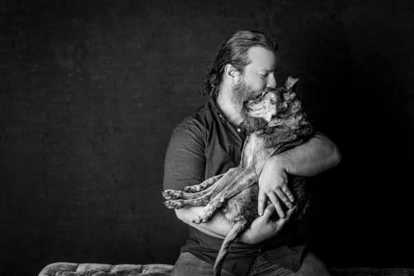 a black and white portrait of a man cradling his dogs in his arms